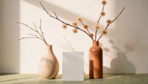 Two ceramic vases with dried branches on a sunlit floor, casting long shadows on a white wall.