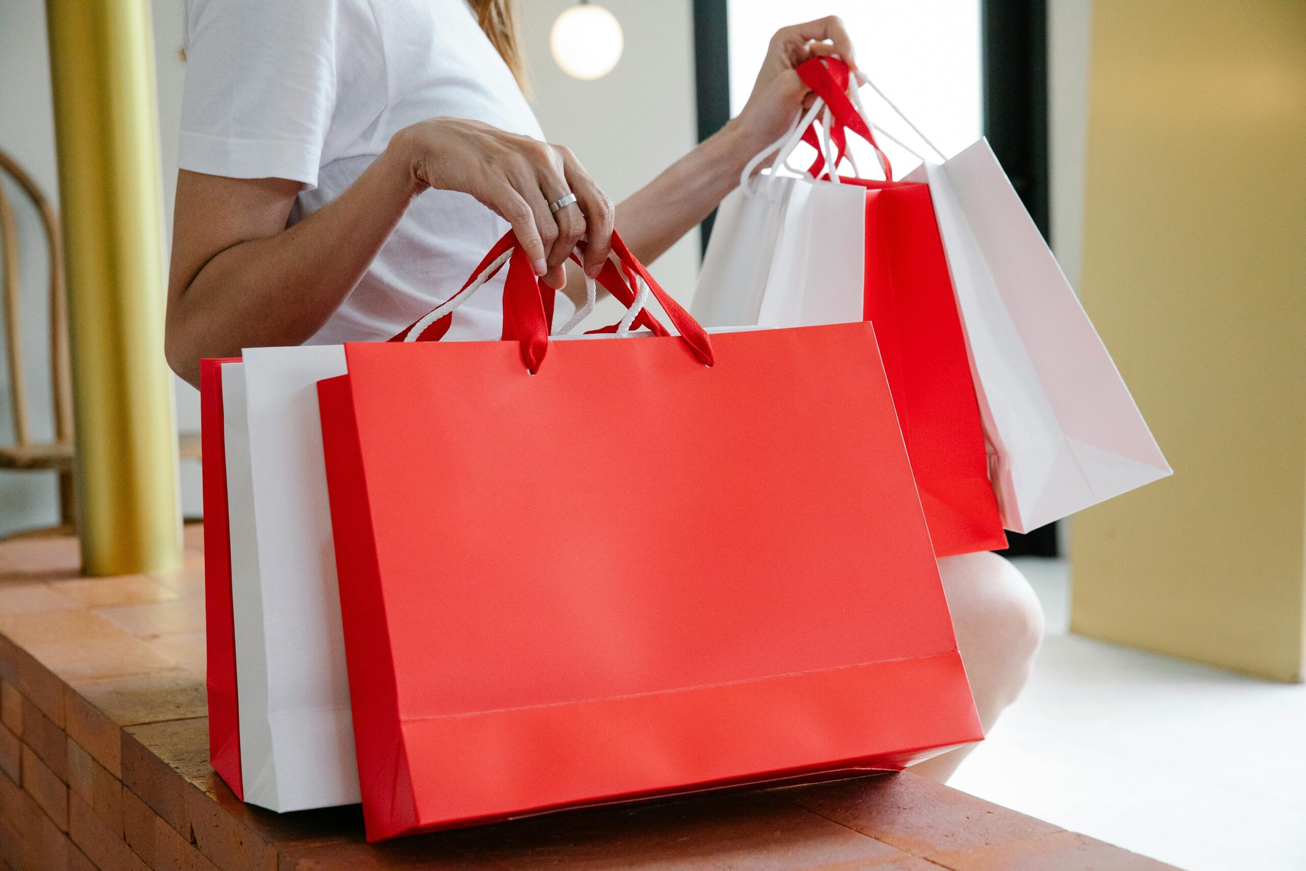 Person holding multiple red and white shopping bags in a mall.