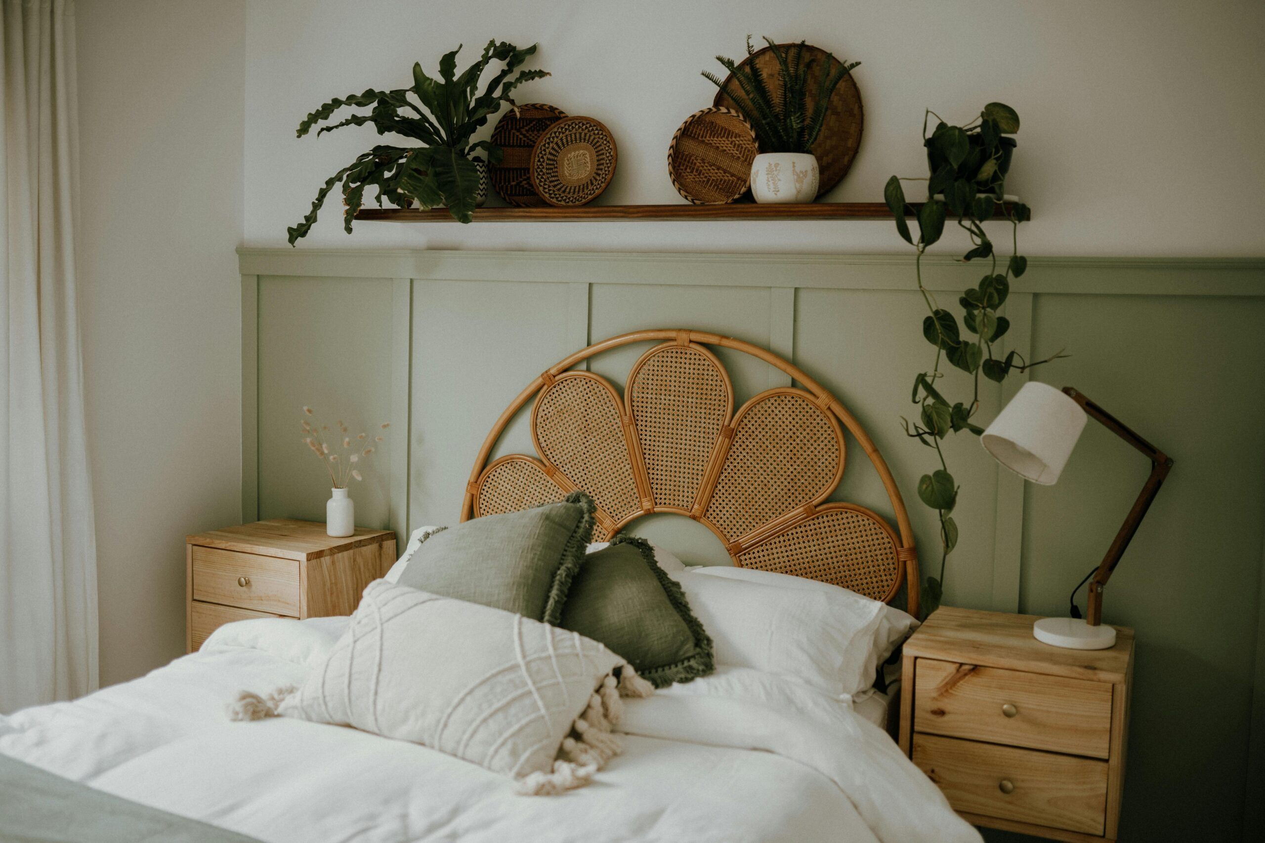 A cosy bedroom with a rattan headboard, matching side tables, green plants, and soft lighting.