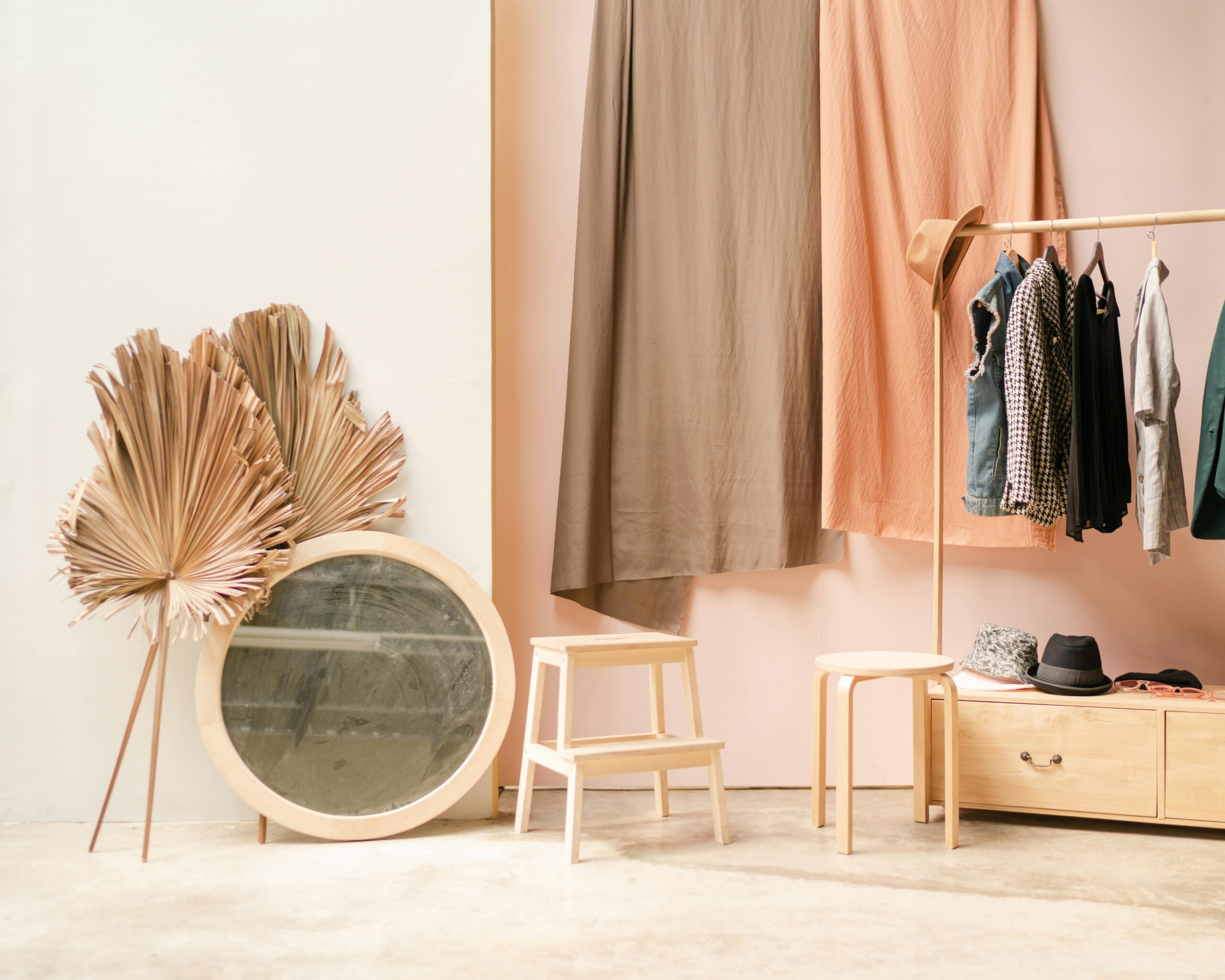 Stylish dressing area with wooden furniture, large leaf-shaped mirror, and colorful hanging clothes.