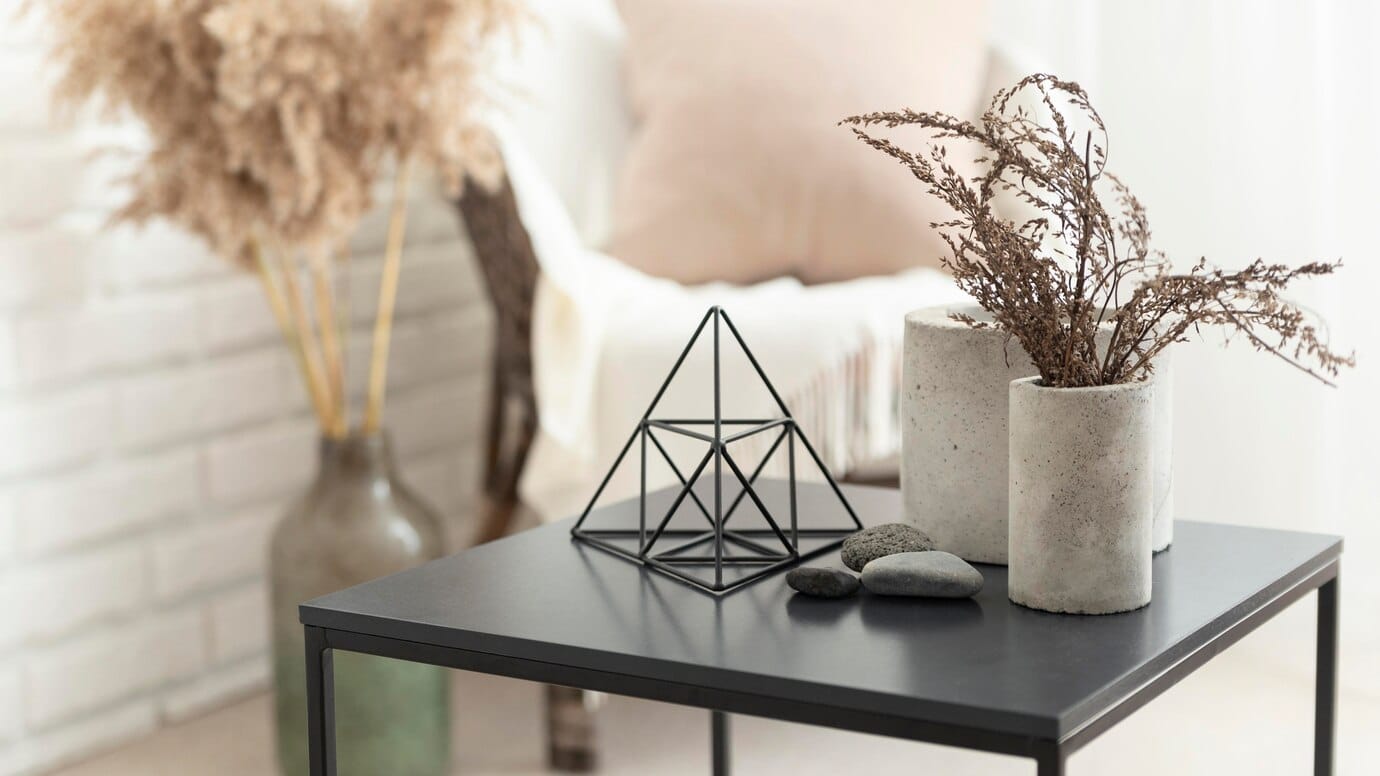 A minimalist living room with dried plants, a geometric sculpture, and pebbles on a coffee table.