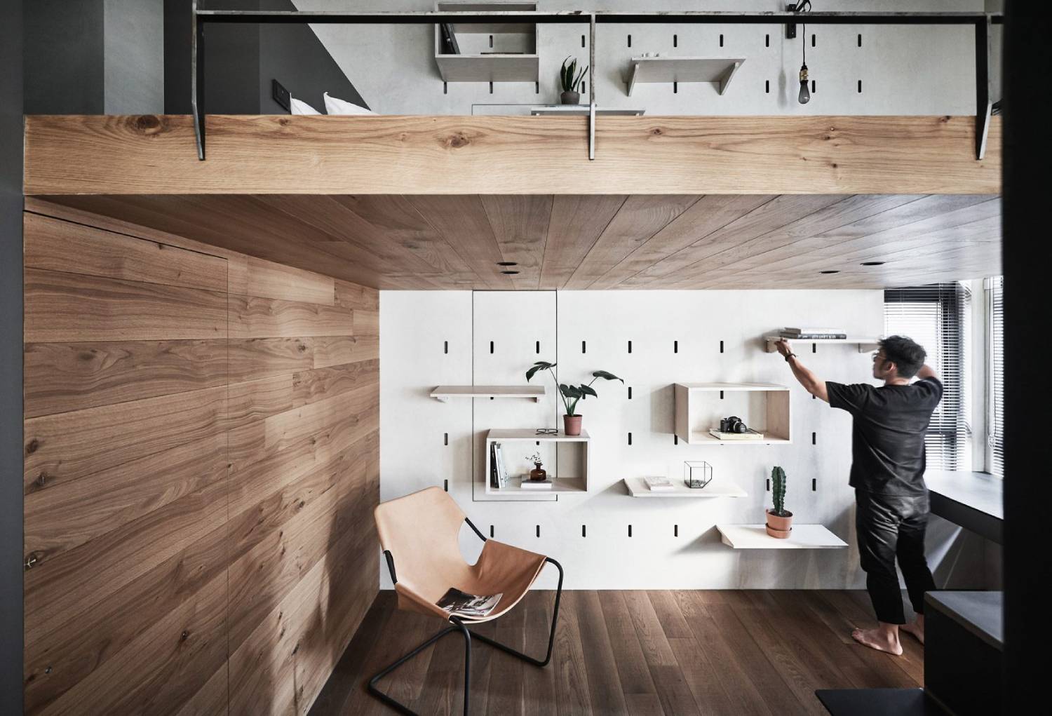  A man arranges a shelf in a modern kitchen with wooden and white decor.