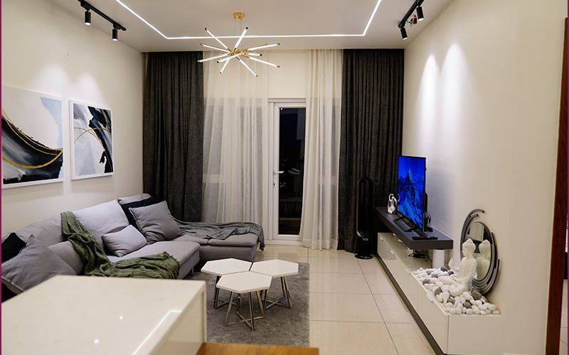Modern living room with grey sofa, starburst chandelier, and decorative white stones near a wall-mounted TV.
