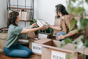 A man and a woman pack books into boxes in a home library.