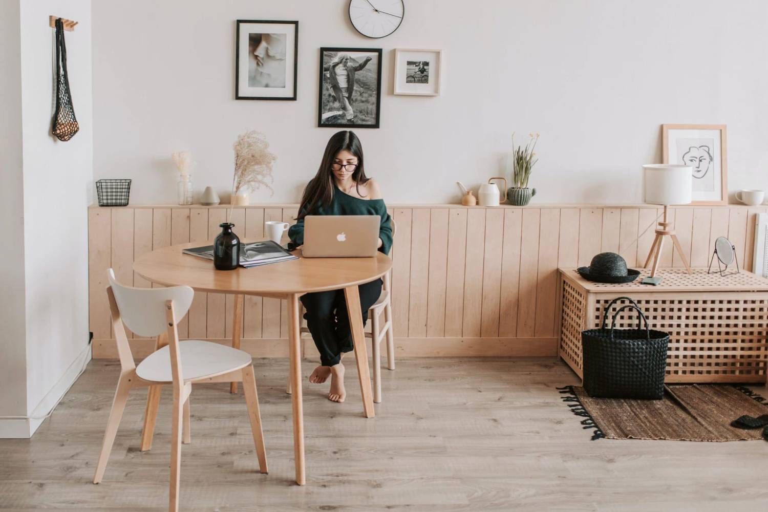Woman working on laptop at wooden table in minimalistic home office with stylish decor.