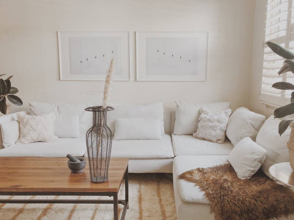 Bright living room featuring a white sectional sofa, wooden coffee table, decorative vases, and minimalist art on the walls.