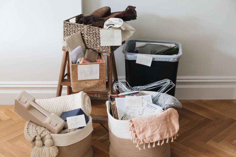 A tidy organizing scene with labeled baskets for recycle, trash, mend, and donate, alongside a bin and various items to sort.