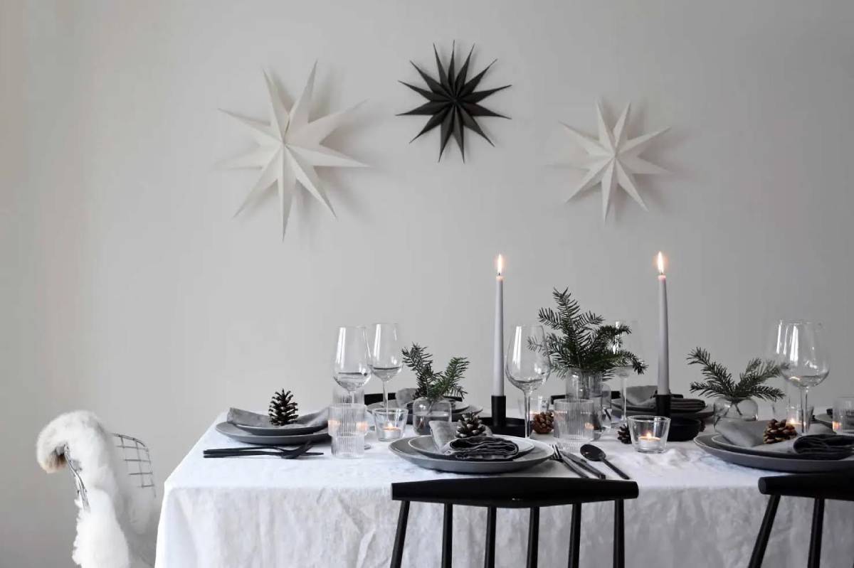 Elegant festive dining table setting with star decorations, candles, and winter greenery on a white tablecloth.