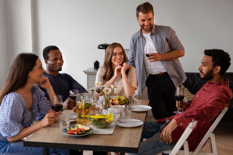Five friends enjoying conversation and drinks around a dinner table in a well-lit room.