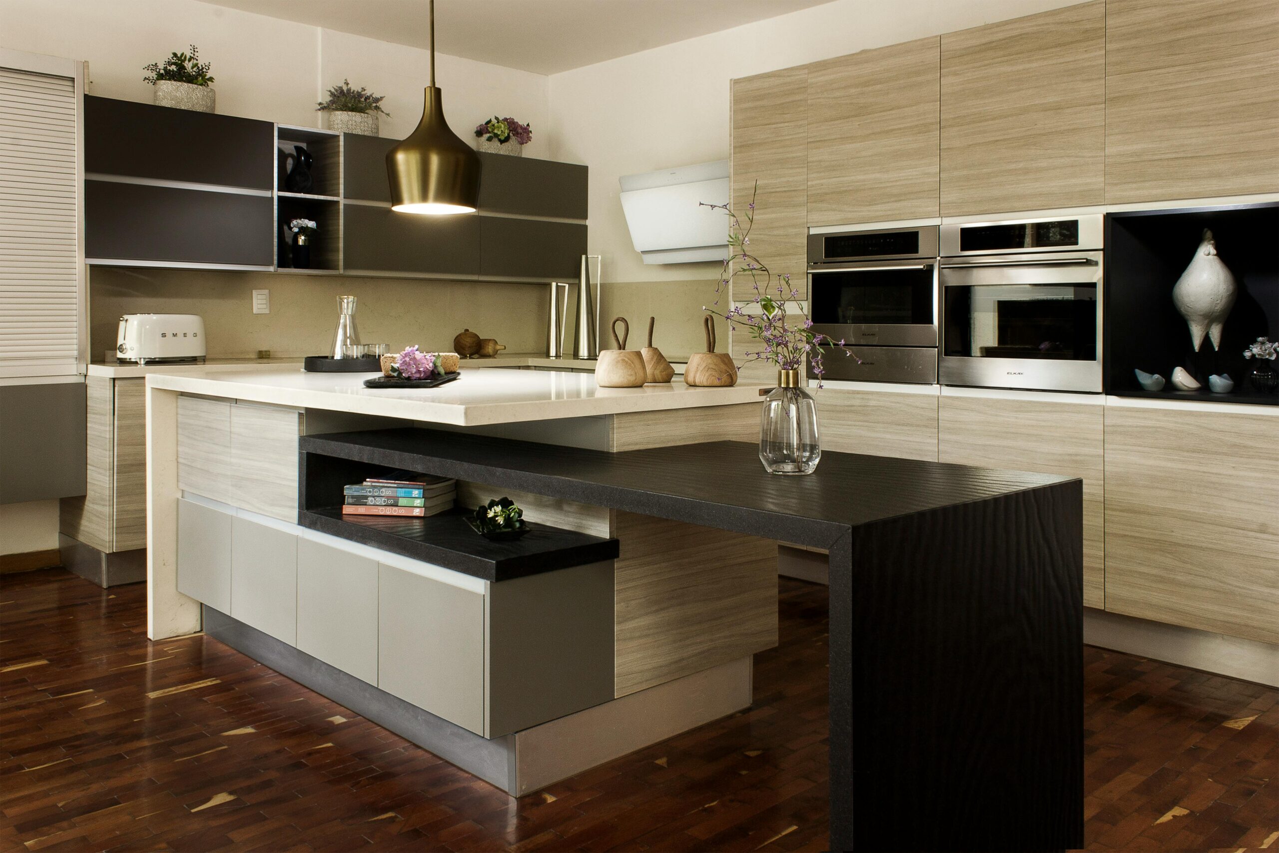 Modern kitchen with wooden cabinets, dark island, built-in appliances, and a pendant light.