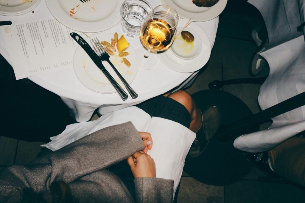 Top-down view of a dinner table with dishes, a glass of wine, and two people holding hands.