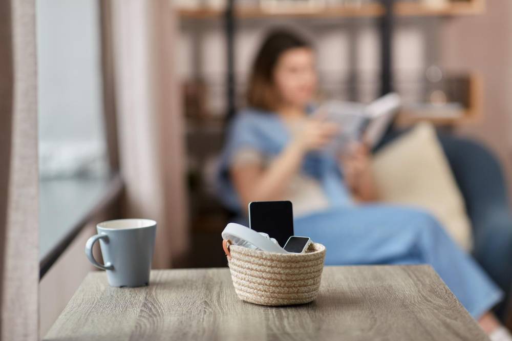  A cosy interior scene with a coffee cup and phone basket on a table, and a woman reading in the background.
