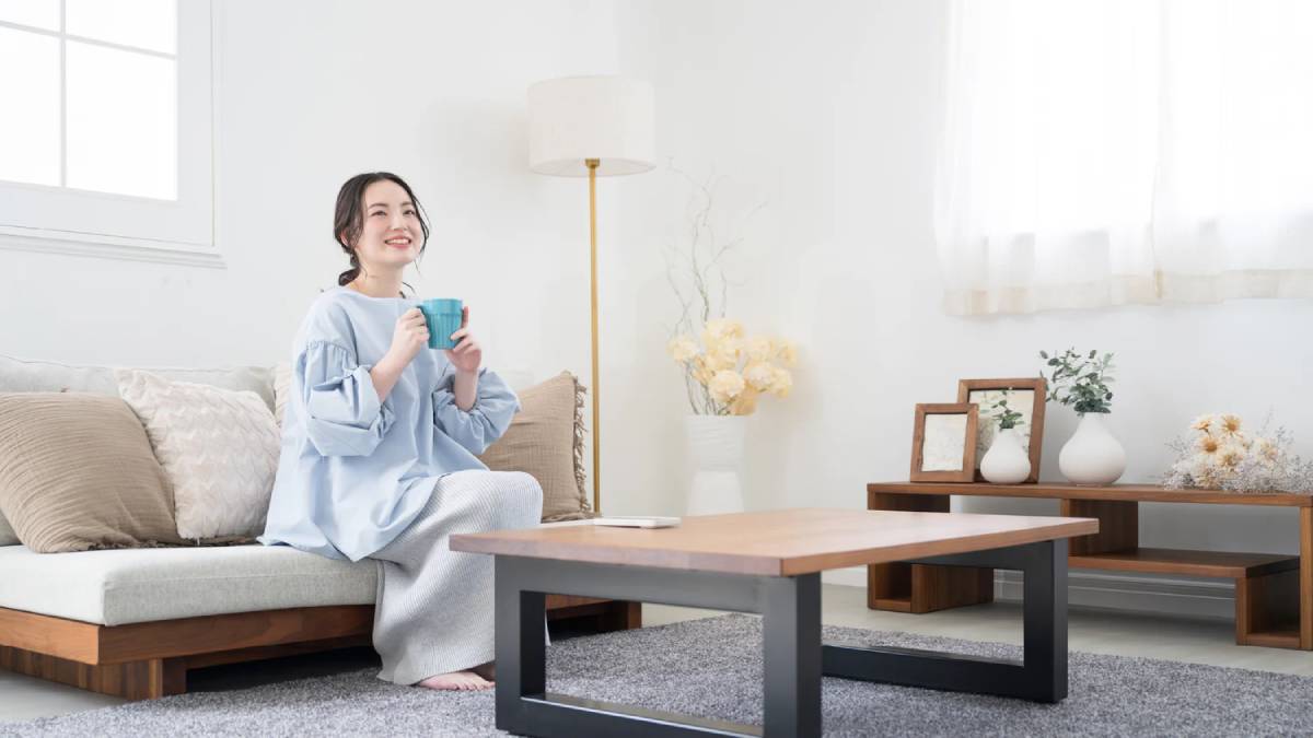 Young woman smiling and holding a mug, sitting on a sofa in a bright living room.