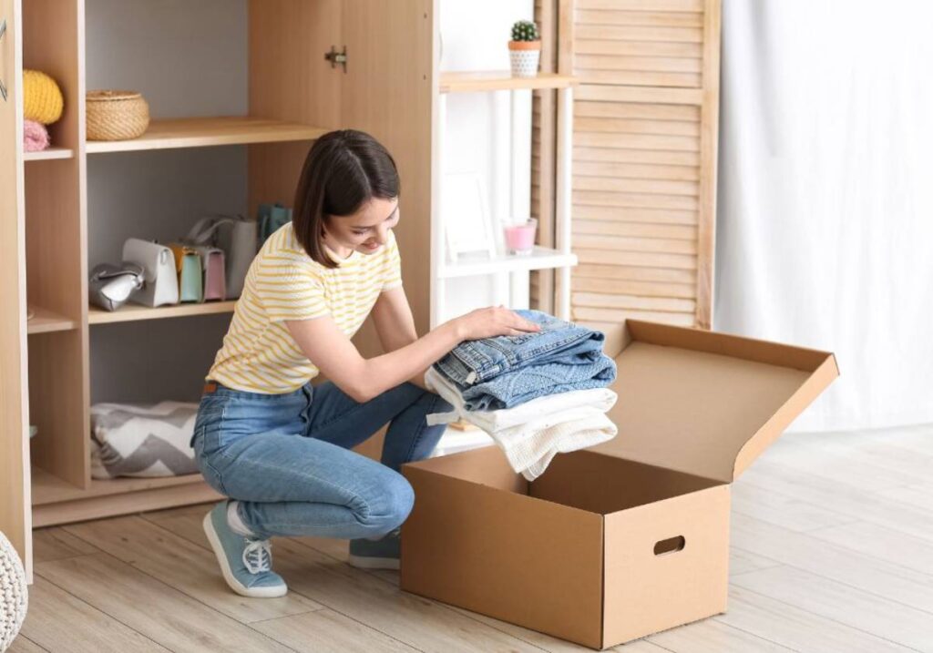 Woman packing clothes into a cardboard box in a tidy room.
