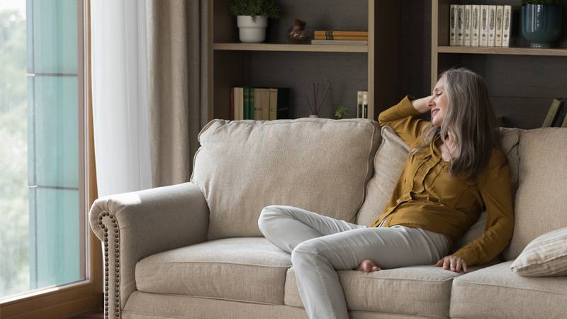  A woman relaxing on a sofa, comfortably lounging and smiling in a well-lit living room.