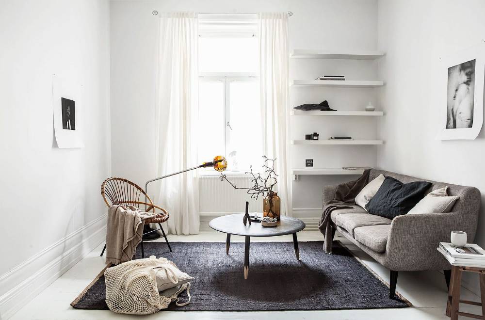  A bright, minimalist living room with a neutral colour palette, featuring a sofa, chair, coffee table, and decorative shelving.