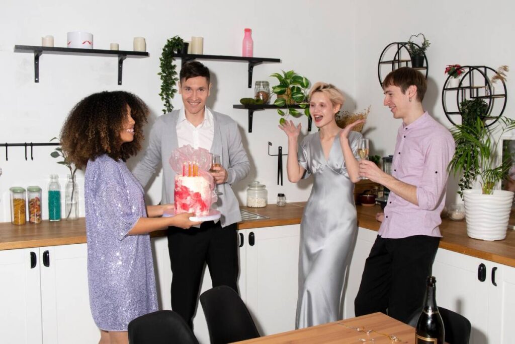 Four friends celebrating with cake and champagne in a modern kitchen.