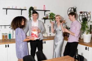 Four friends celebrating with cake and champagne in a modern kitchen.