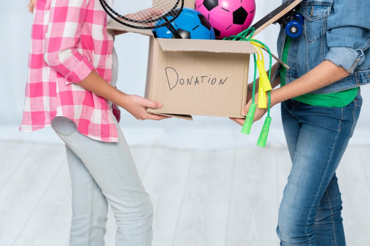 Two children holding a donation box filled with sports equipment.