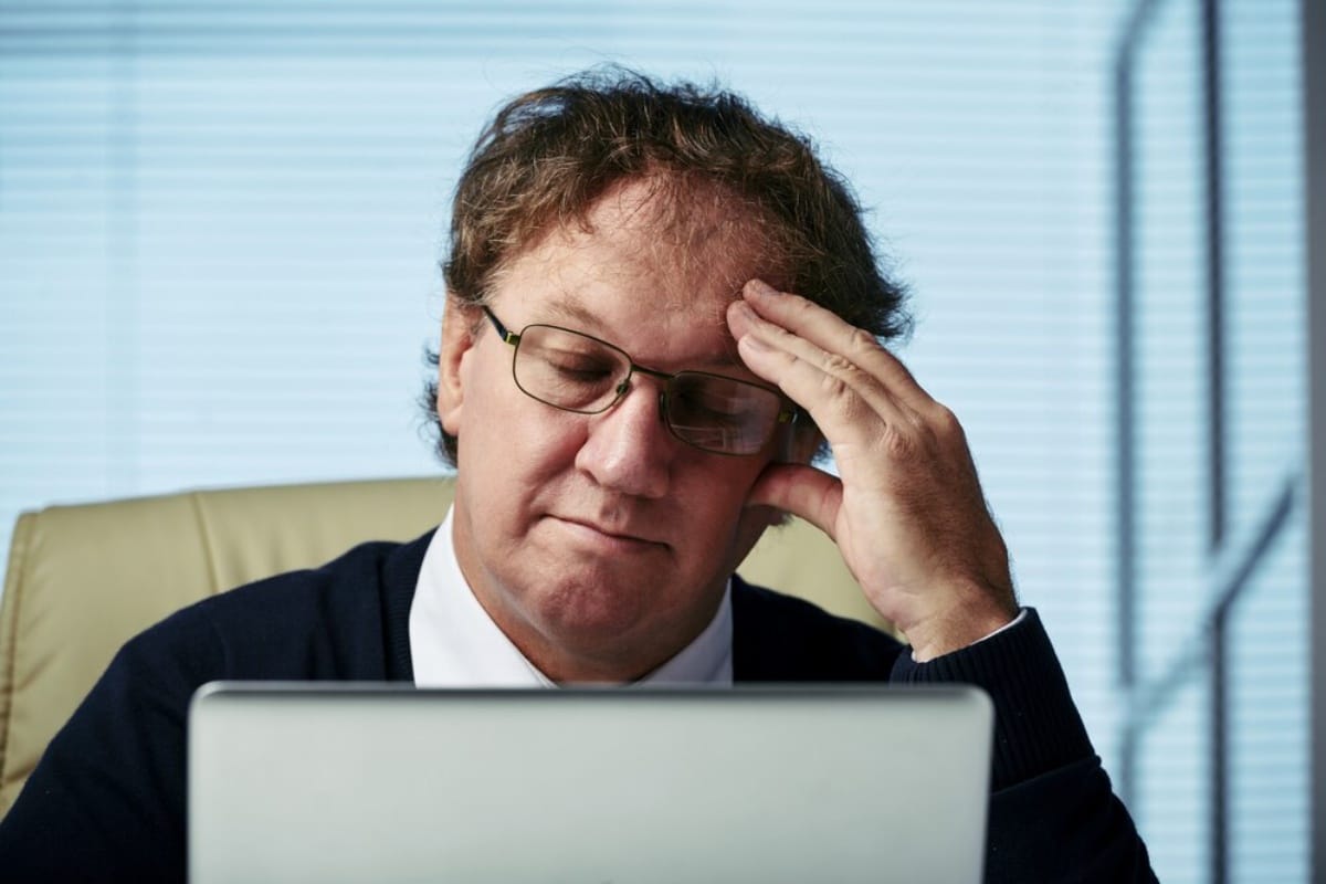 Middle-aged man looking stressed while working on a laptop in an office setting.