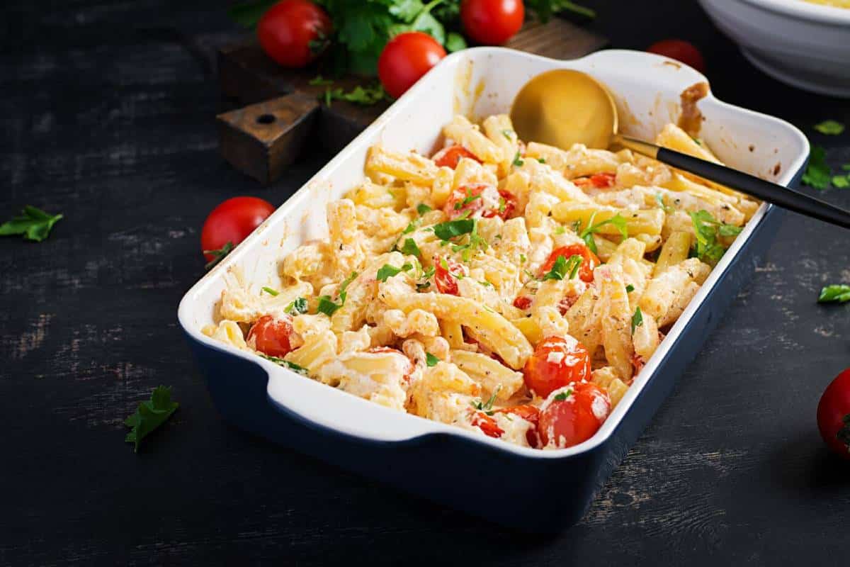 Baked pasta with tomatoes and herbs in a white casserole dish on a dark wooden table.