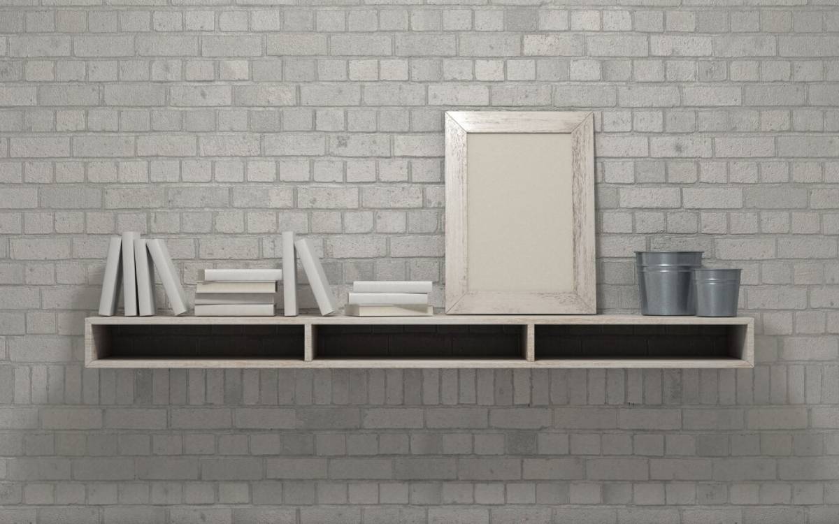  A minimalist shelf arrangement featuring books, a vintage frame, and metal buckets against a grey brick wall.