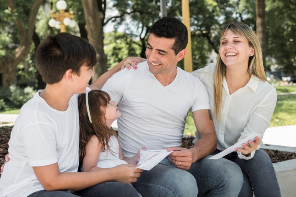 Family with two adults and two children enjoying time together in a park, smiling and interacting lovingly.