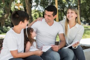 Family with two adults and two children enjoying time together in a park, smiling and interacting lovingly.