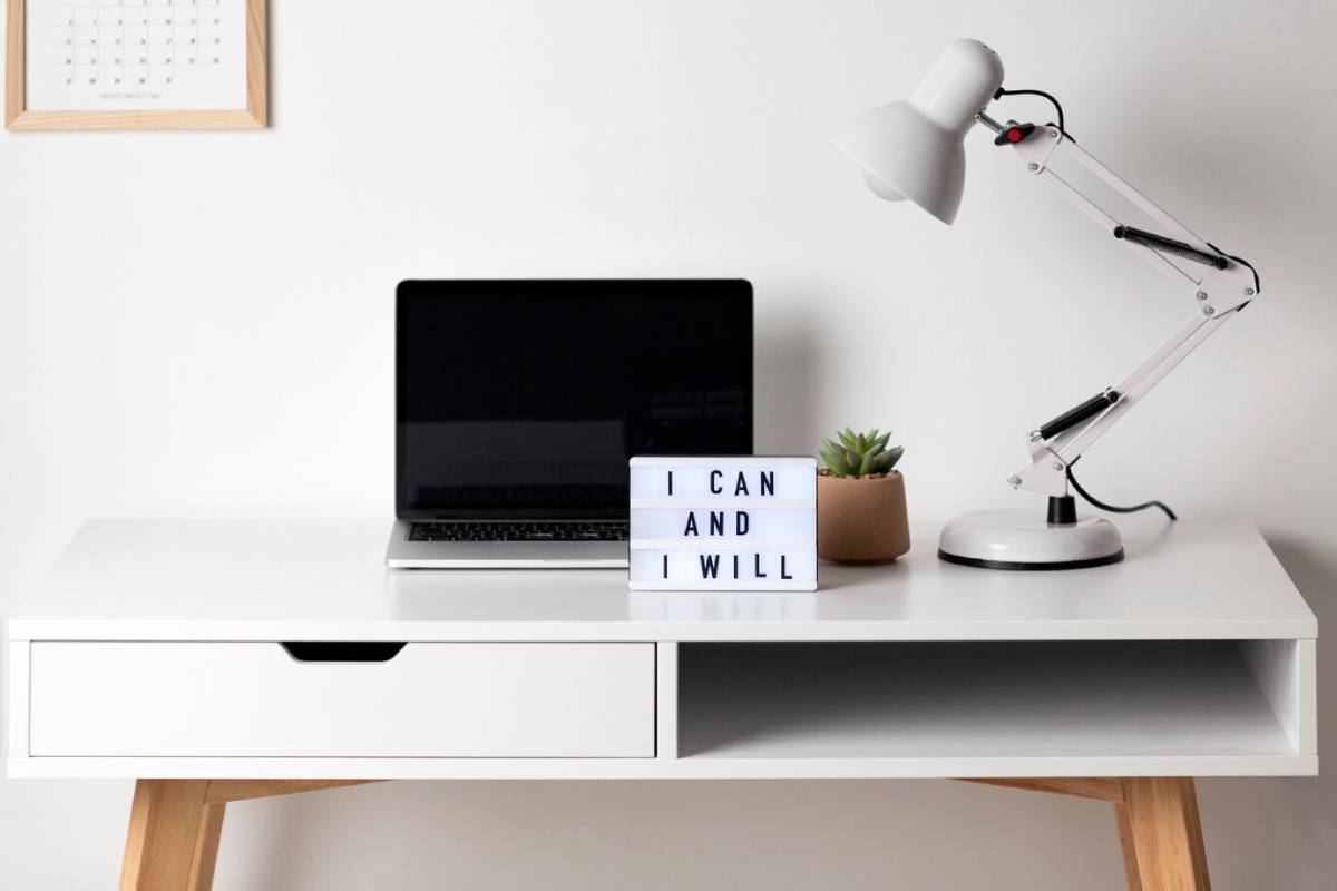 A minimalist desk featuring a laptop, a motivational lightbox stating I CAN AND I WILL, a potted succulent, and a lamp.